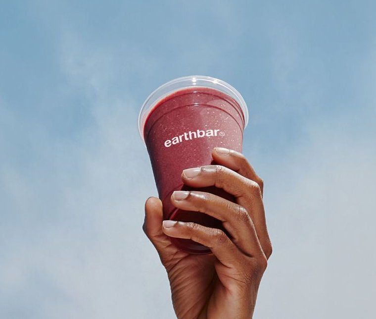 Pink Earthbar smoothie held against a blue sky